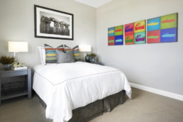 A new bedroom with a white bed featuring colorful throw pillows ans colorful artwork on the walls.