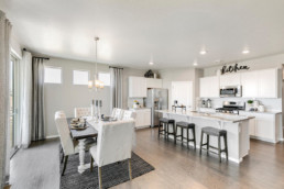 A dining and room and kitchen of a new home, decorated in white accents, featuring a large island.