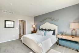 A large master bedroom with a grey wall, white bed and a beautiful metal art piece on the wall.