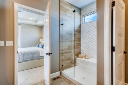 A contemporary ensuite bathroom featuring a shower with a wooden wall and white tile backsplash.
