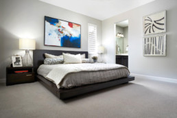 A large king size bed in a master bedroom with a beautiful colorful painting on the wall.